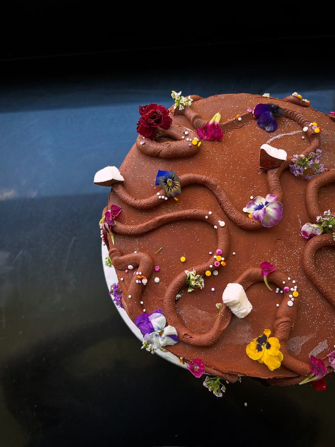 Artisan chocolate cake decorated with edible flowers and pearl sprinkles